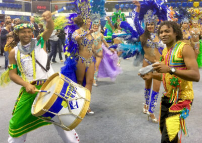 2 hommes jouant des percussions et danseuses, tous en tenue de fête brésilienne